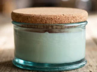 Flat round glass jar candle with a cork lid, low pale green soy candle in blue-green recycled glass on a wooden table