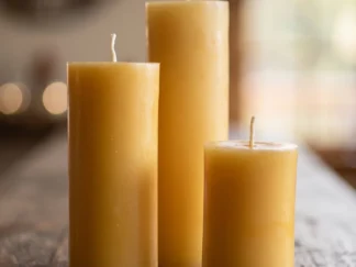Three pure beeswax pillar candles in different heights, natural golden yellow and unscented, on a rustic wooden table