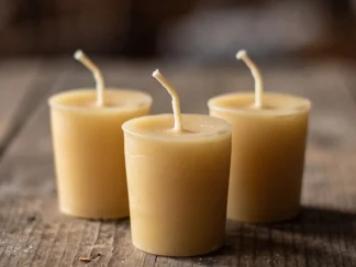 Three pure beeswax votive candles in natural pale gold with white wicks on a weathered wooden table